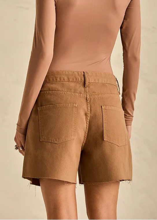 Woman wearing a brown long-sleeve top and shorts against a beige marble wall.