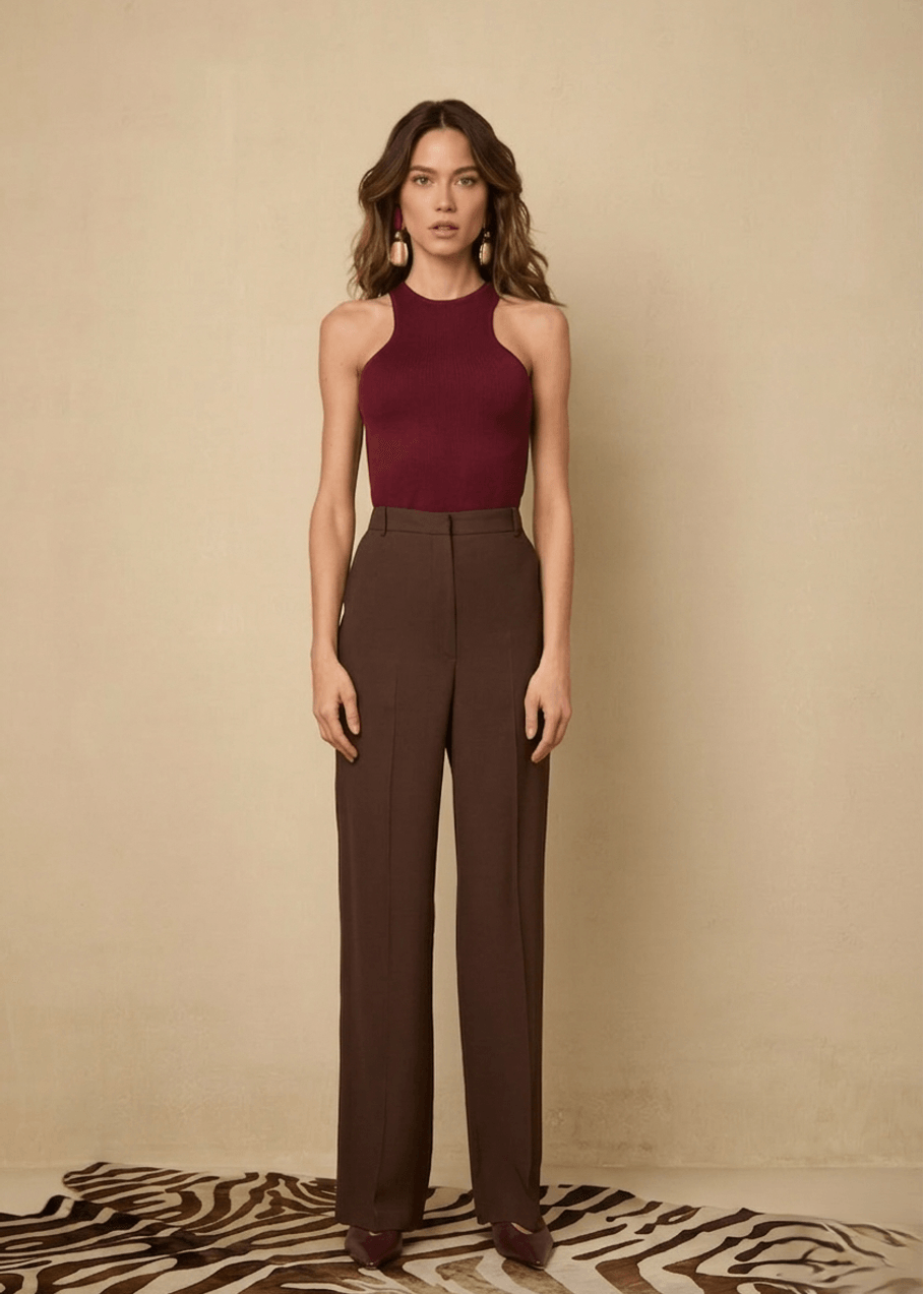 Woman wearing a burgundy top and brown pants against a beige background