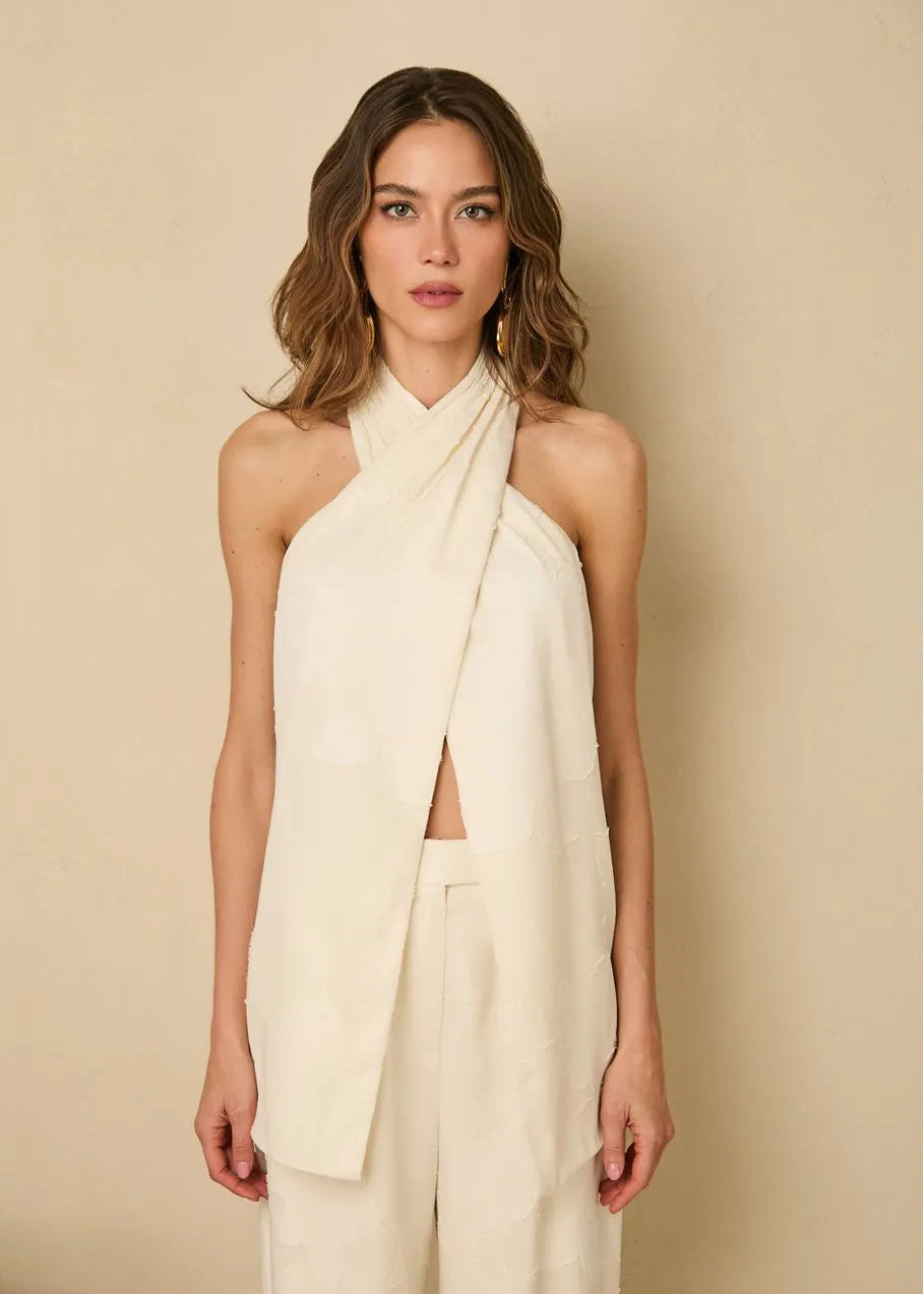 Woman wearing a cream-colored halter top and wide-leg pants against a beige background