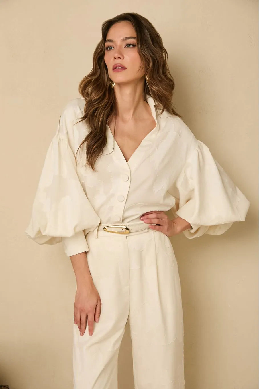 Woman wearing a white outfit with wide sleeves against a beige background