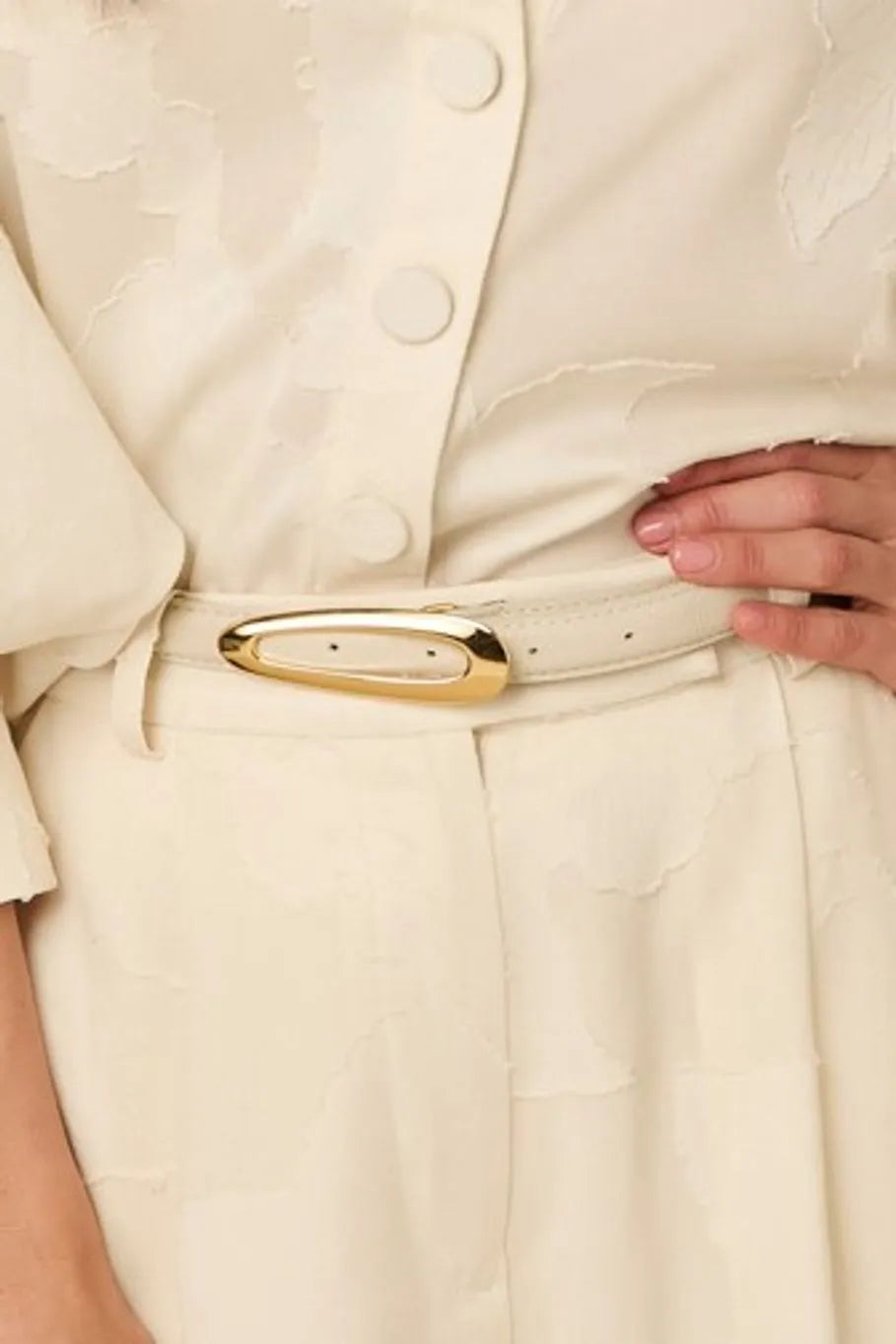 Close-up of a person adjusting a off white belt on a beige outfit.