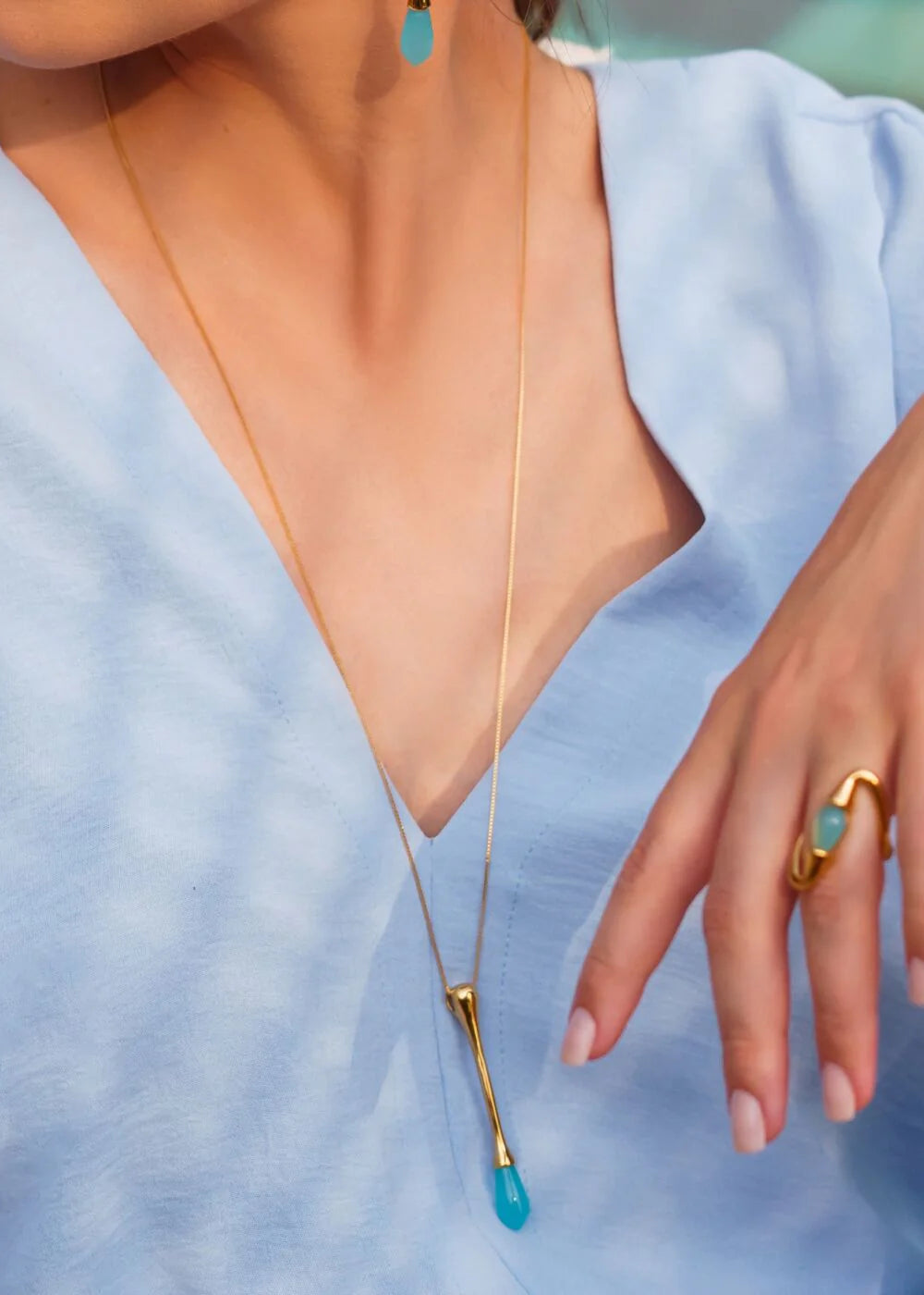 Close-up of a necklace with a blue pendant and a gold ring on a light blue background