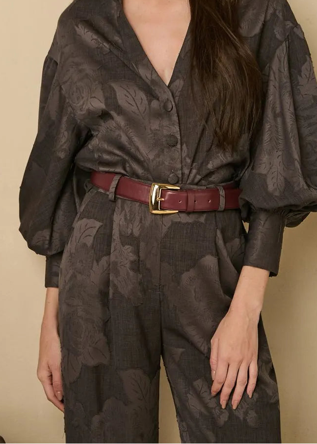 Woman wearing a dark floral patterned outfit with a red belt against a beige background