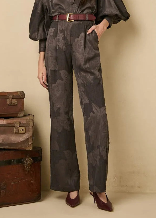 Woman in a dark gray outfit standing next to vintage suitcases against a beige wall.