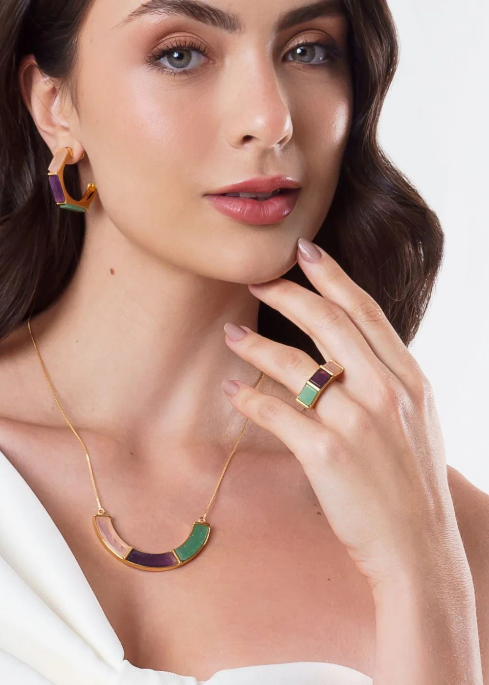 Woman wearing gold jewelry with green and purple accents on a white background
