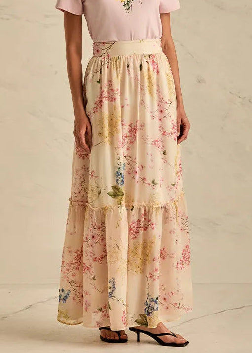 Woman wearing a pink top with floral design and a long floral skirt on a neutral background