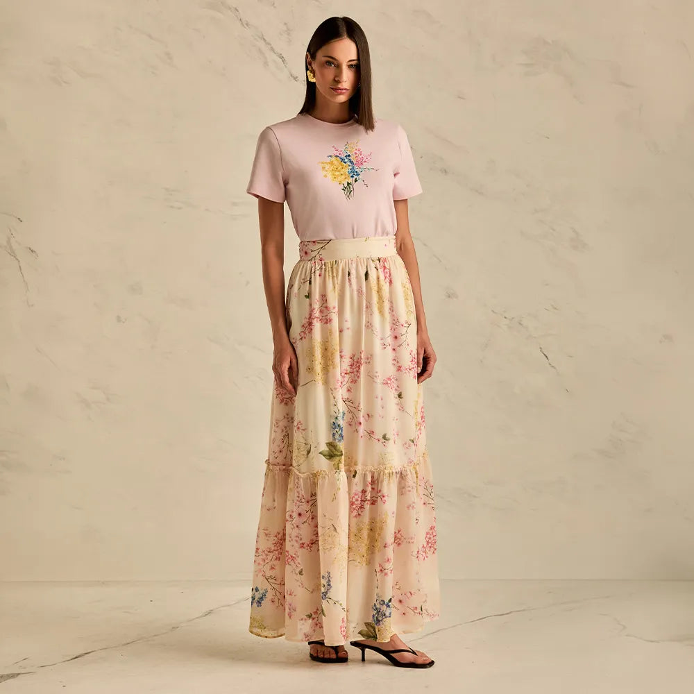 Woman wearing a pink top with floral design and a long floral skirt on a neutral background