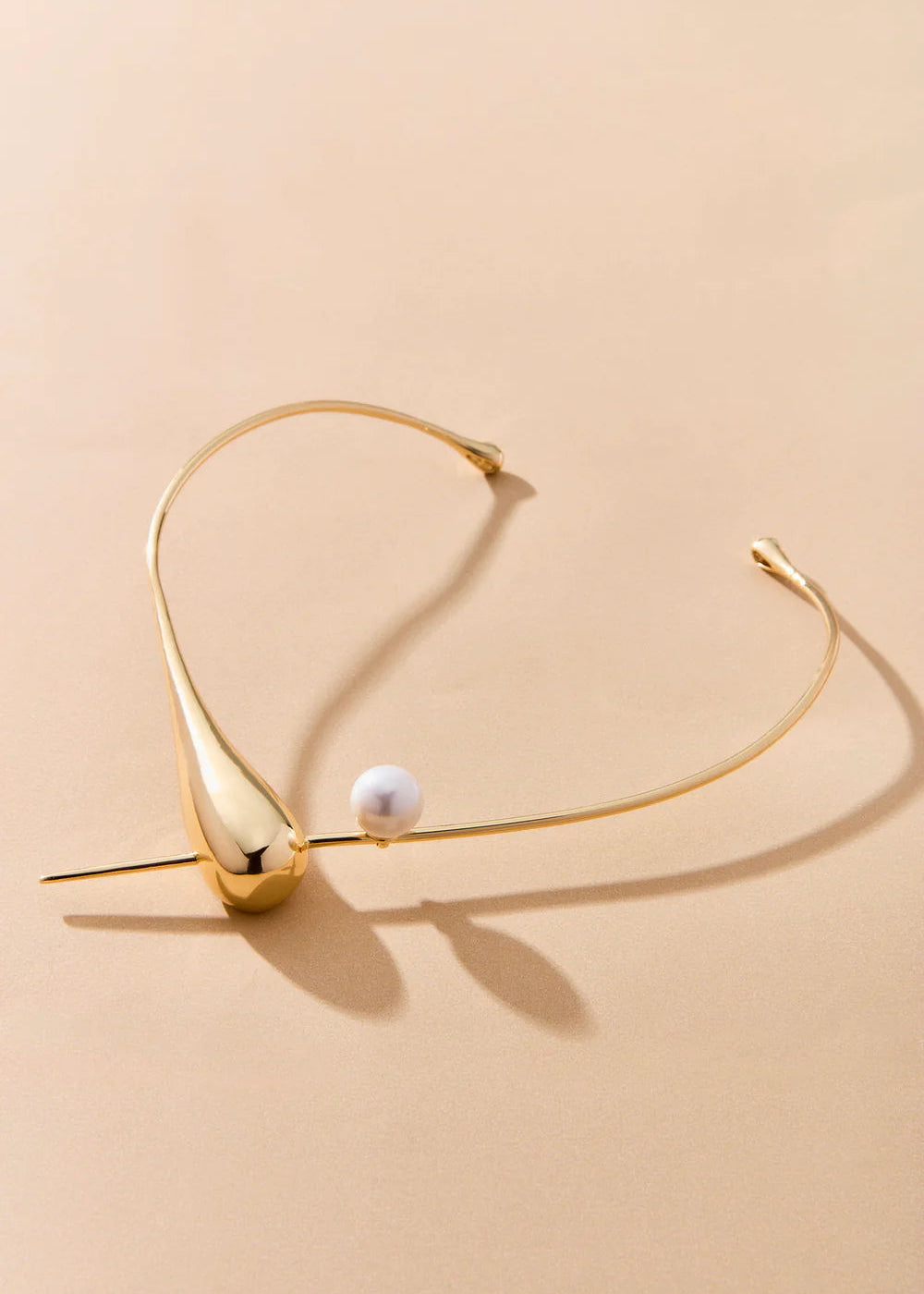 Gold necklace with a pearl on a beige background