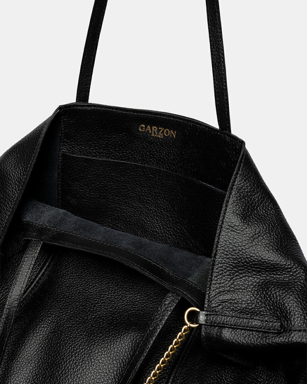 Black leather bag with gold zipper and 'GARZON' branding on a light gray background