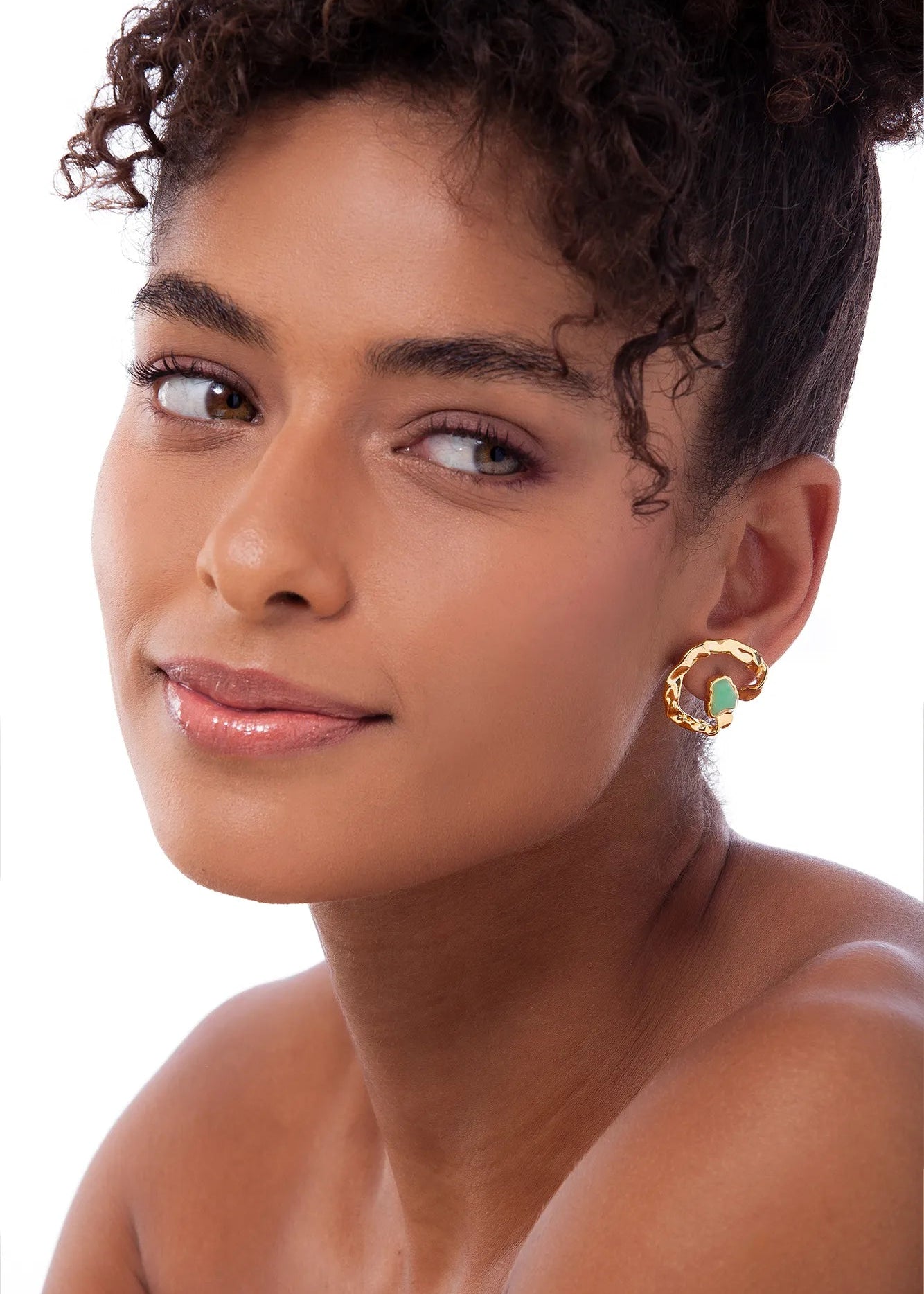 Woman wearing gold hoop earrings with green stones on a white background