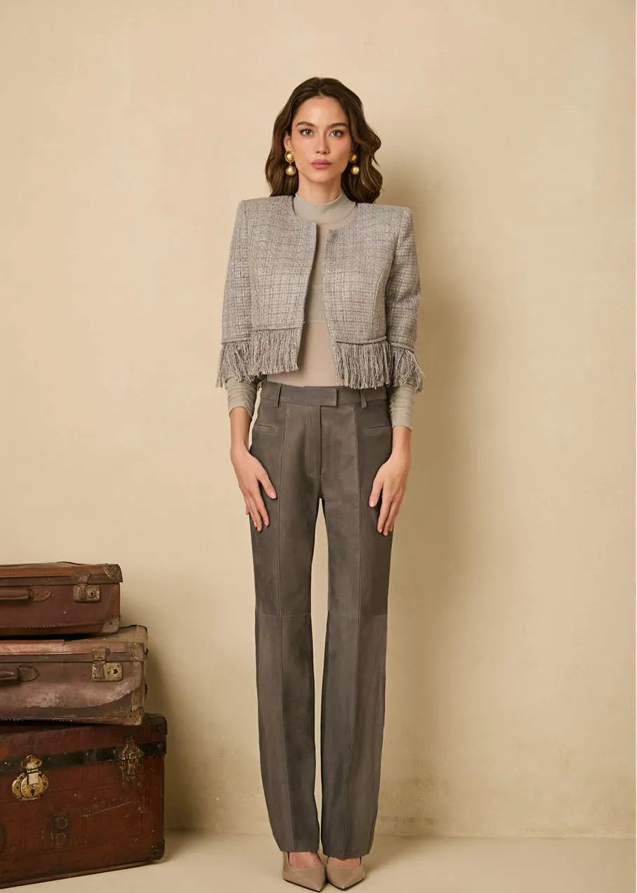 Woman wearing a gray textured jacket and pants standing next to vintage suitcases on a beige background