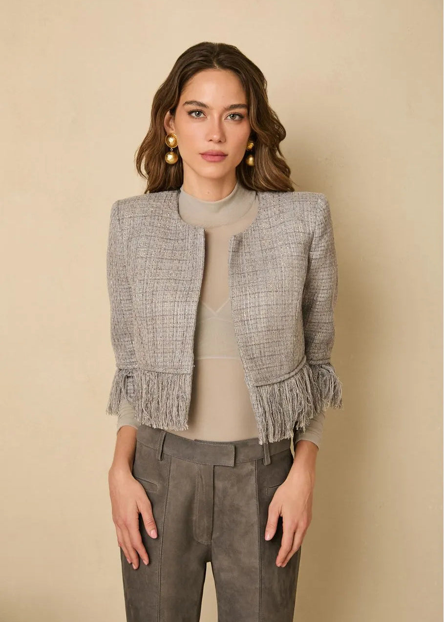 Woman wearing a gray tweed jacket with fringes on a beige background