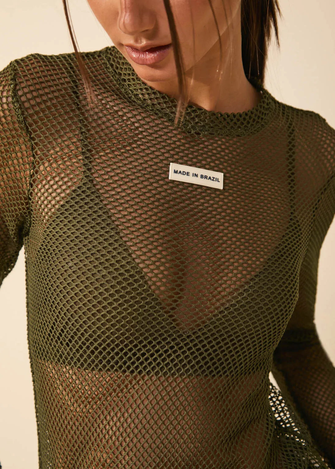 Person wearing a green fishnet top with 'Made in Brazil' label on a neutral background