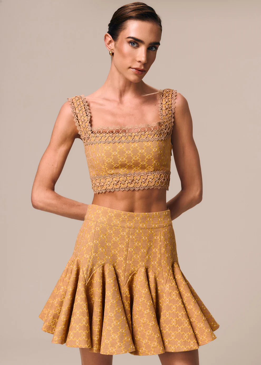 Woman wearing a mustard yellow dress with lace details on a beige background