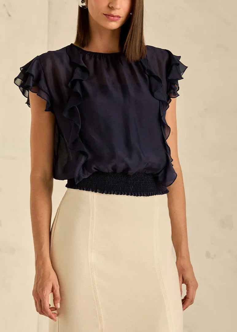 Woman wearing a navy blue blouse with ruffled sleeves against a beige background