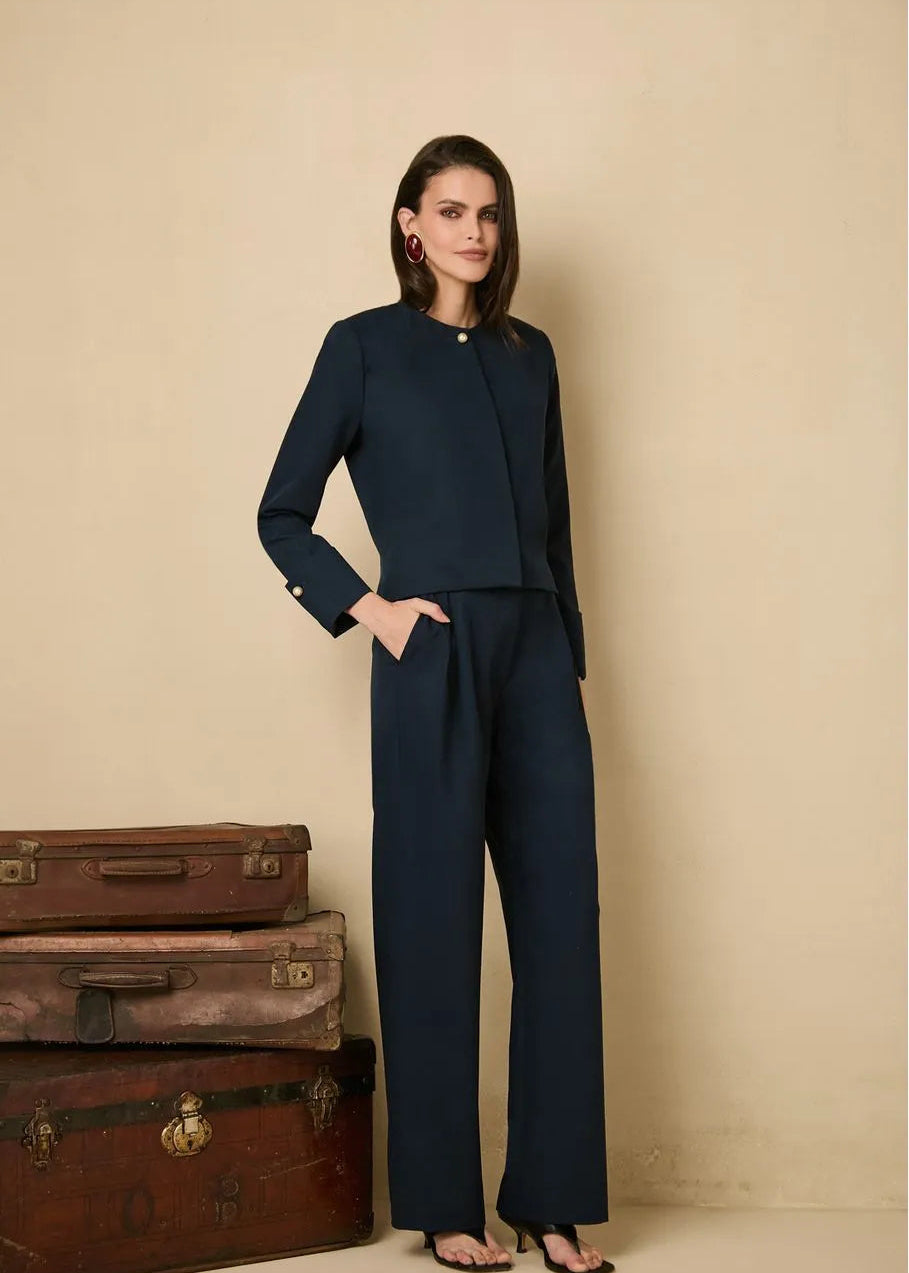 Woman in a navy suit standing next to vintage trunks against a beige wall