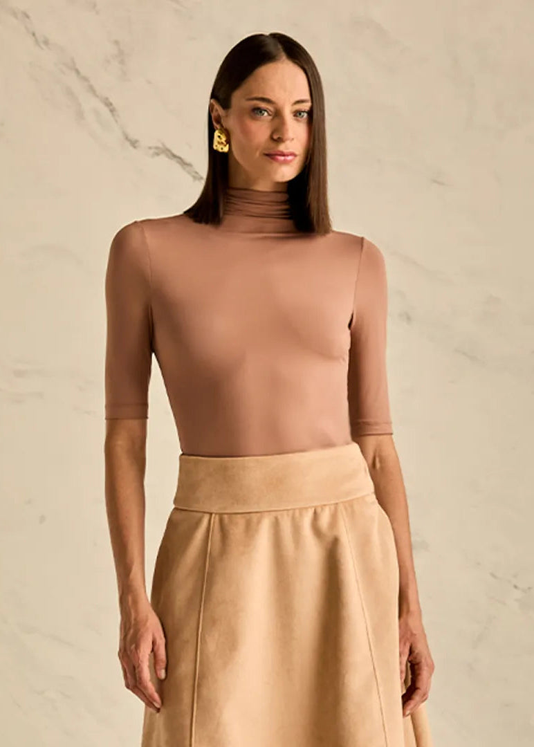 Woman wearing a beige turtleneck top and skirt against a neutral background