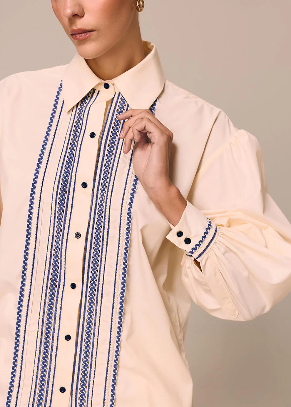 Close-up of a cream-colored shirt with blue embroidery on a neutral background