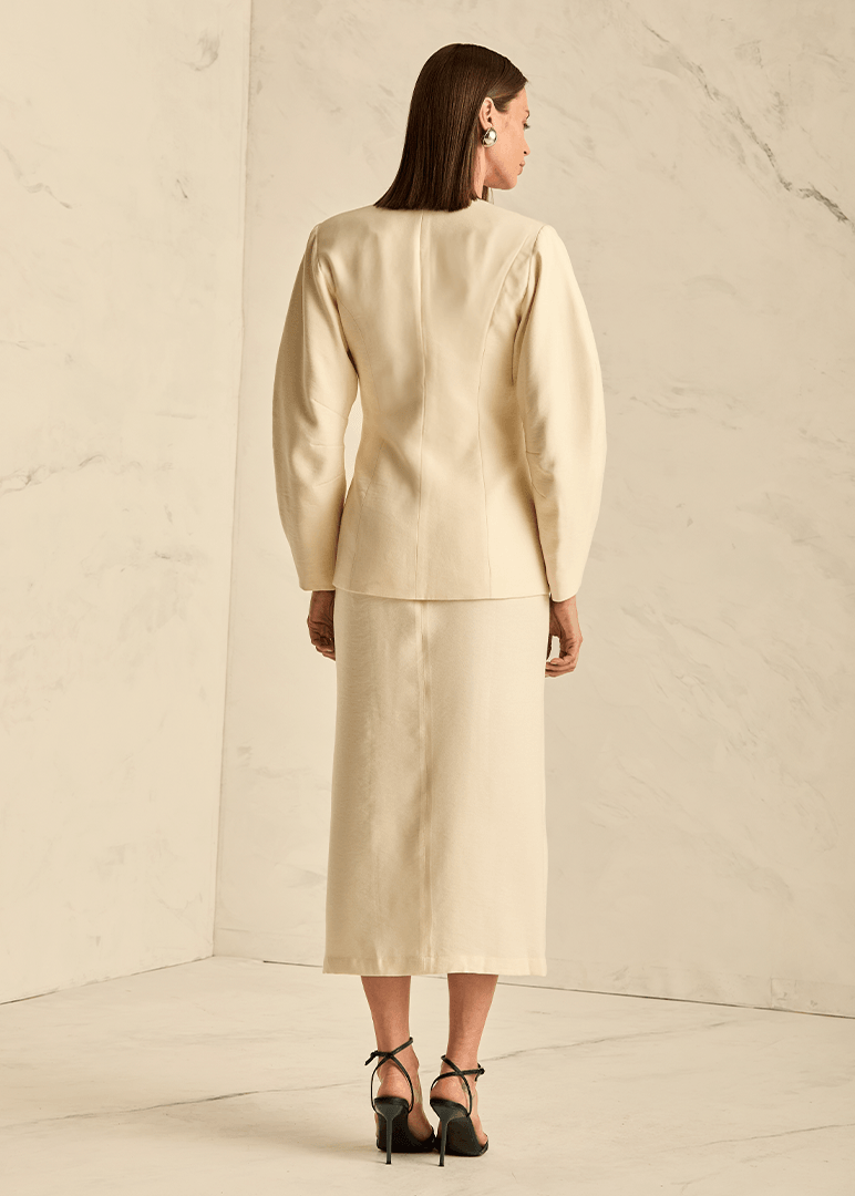 Woman wearing a beige suit standing in a minimalistic room with a marble wall.