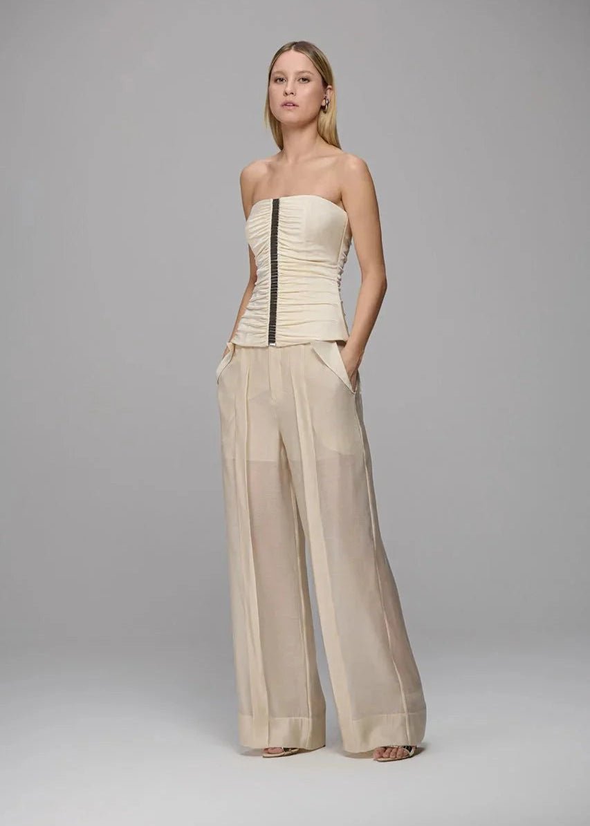 Woman wearing a beige strapless top and wide-leg pants on a gray background