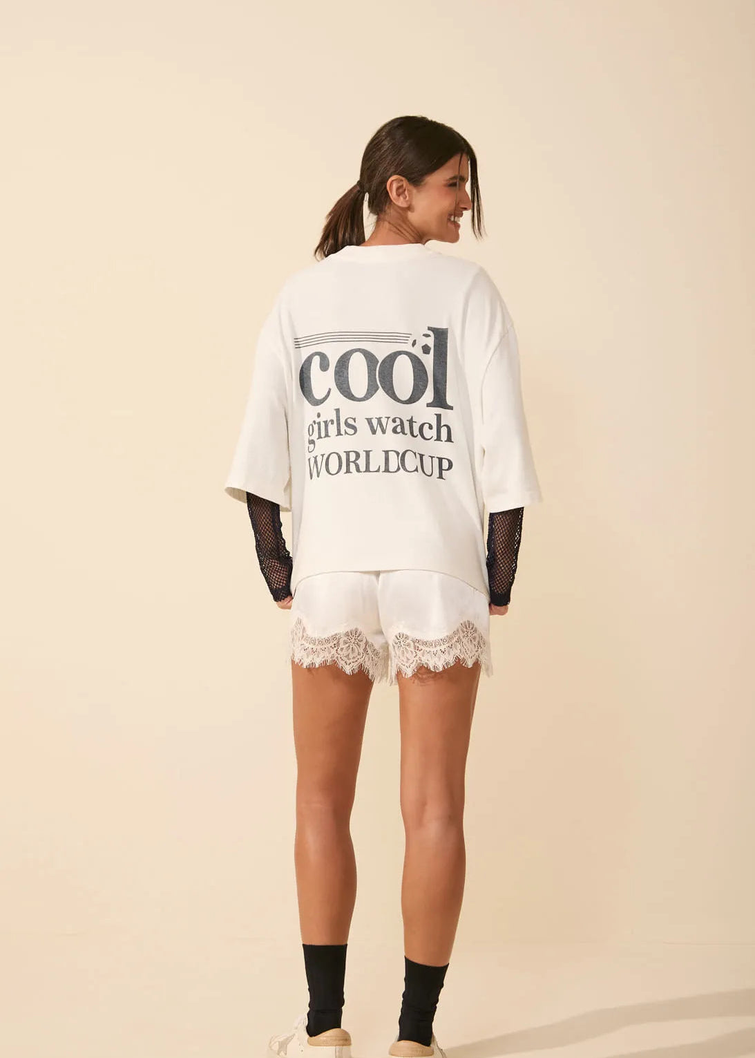 Woman wearing a white oversized t-shirt with text and lace shorts on a beige background