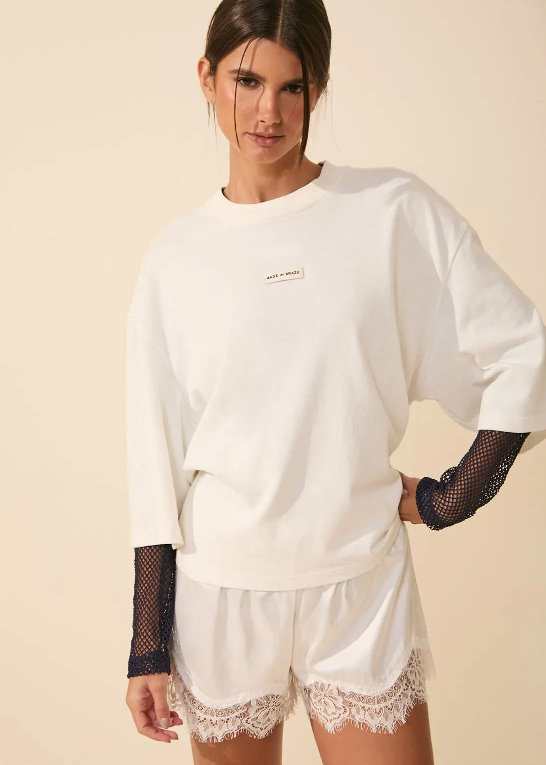 Woman wearing a white oversized sweatshirt and lace shorts on a beige background