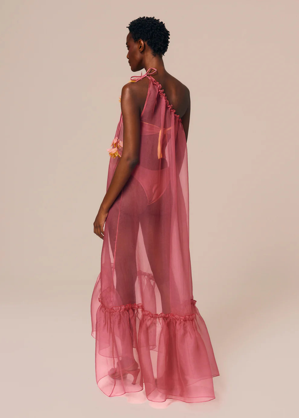 Woman wearing a pink sheer dress with ruffled layers on a beige background