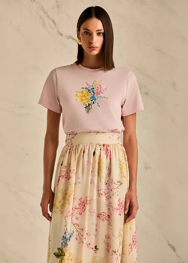 Woman wearing a pink t-shirt with floral design and a floral skirt on a neutral background