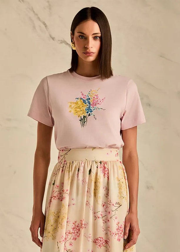 Woman wearing a pink t-shirt with floral design and a floral skirt on a neutral background