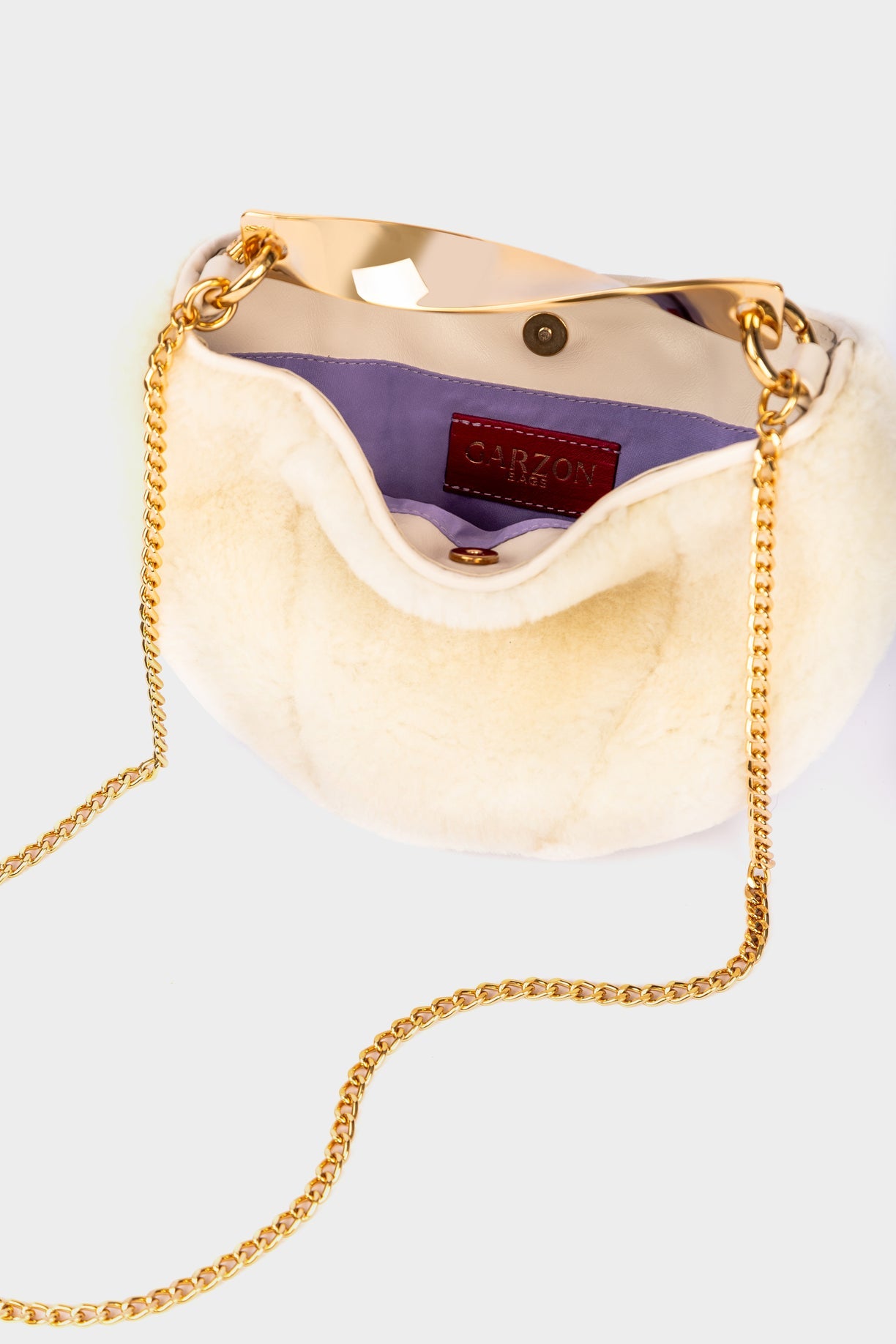 A cream-colored crescent handbag with a gold-tone chain strap and a purple interior lining, shown against a light gray background.
