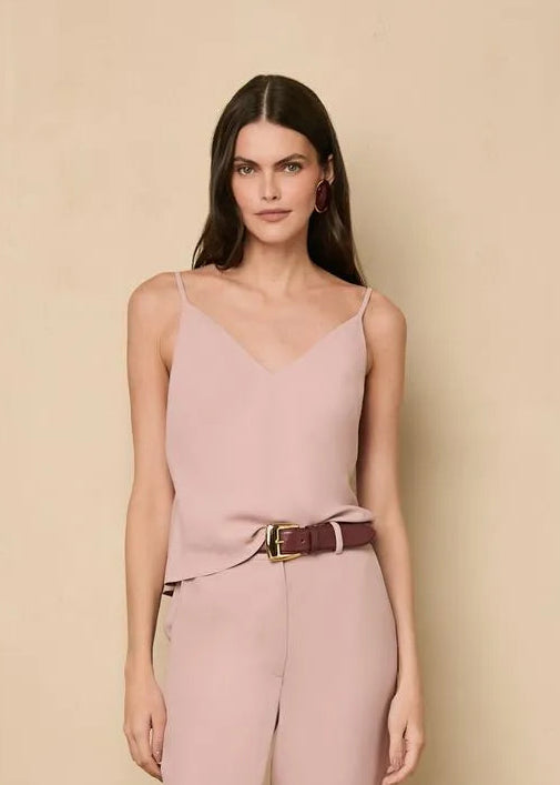 Woman wearing a pink tank top with a belt against a beige background