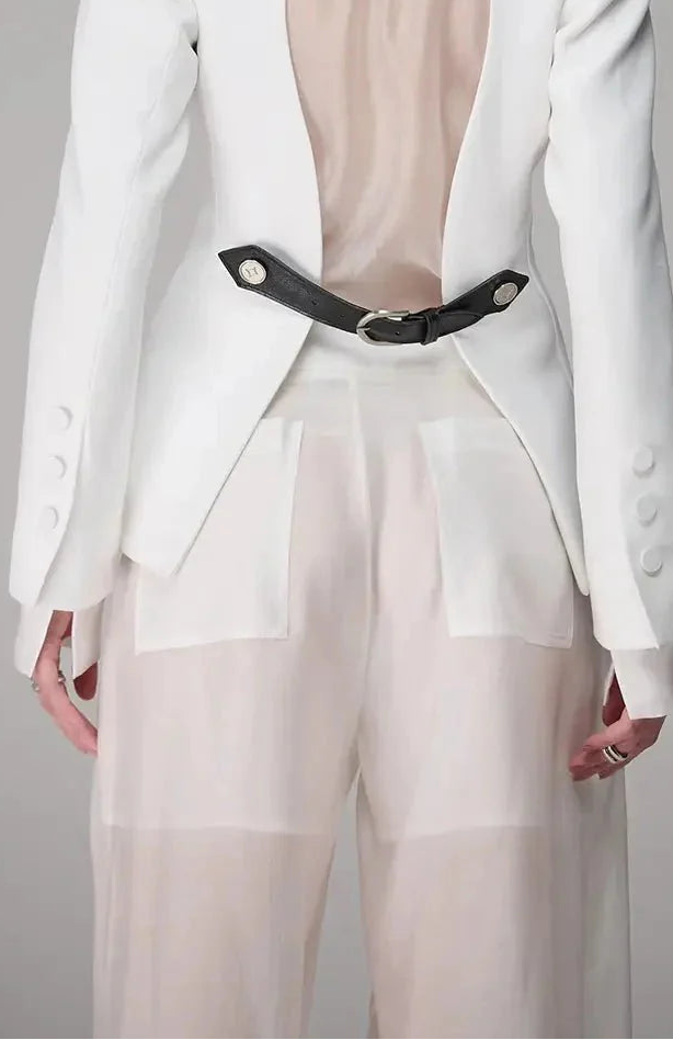 White blazer with sheer panels and a black belt on a gray background