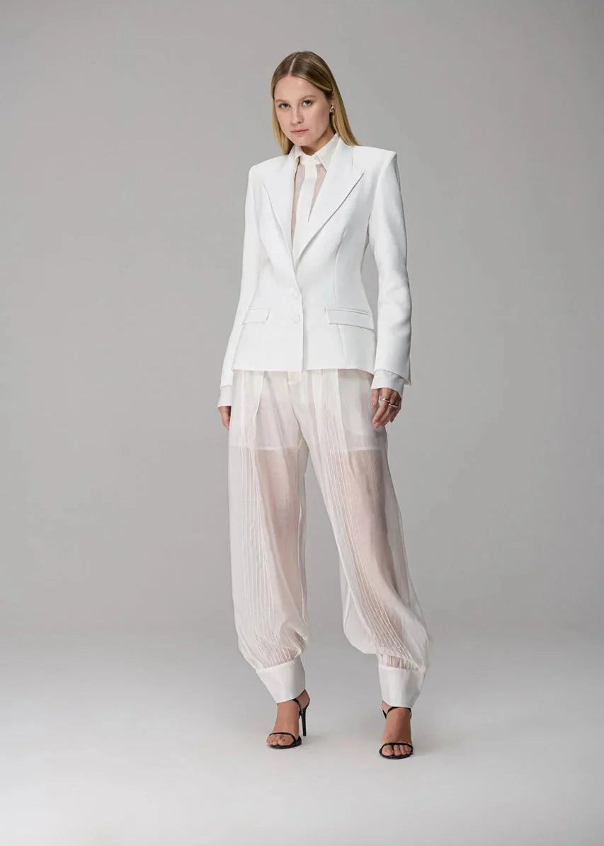 Woman wearing a white suit with sheer pants on a gray background