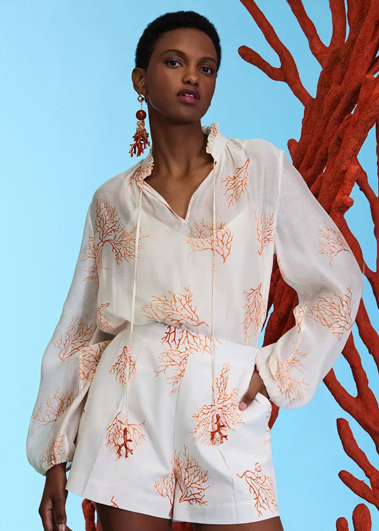 Woman wearing a white outfit with coral patterns standing next to red coral against a blue background