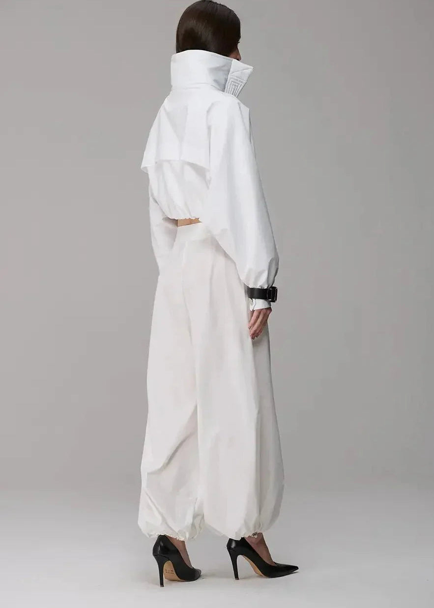 Person wearing a white outfit with a high collar on a gray background