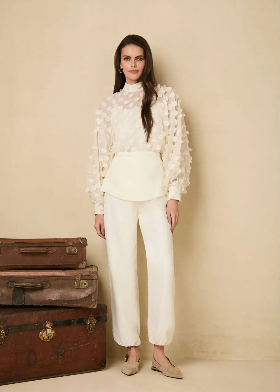 Woman in a white outfit standing next to vintage suitcases against a beige wall