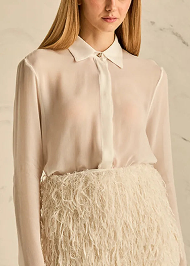 Woman wearing a light-colored blouse and skirt against a neutral background