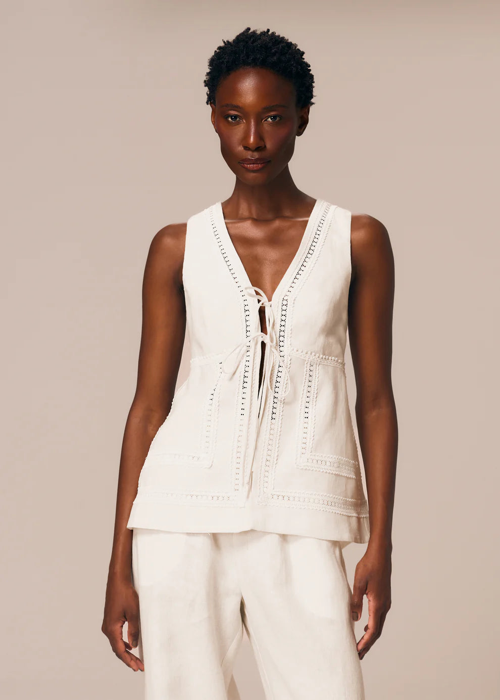 Woman wearing a white sleeveless top and pants against a beige background