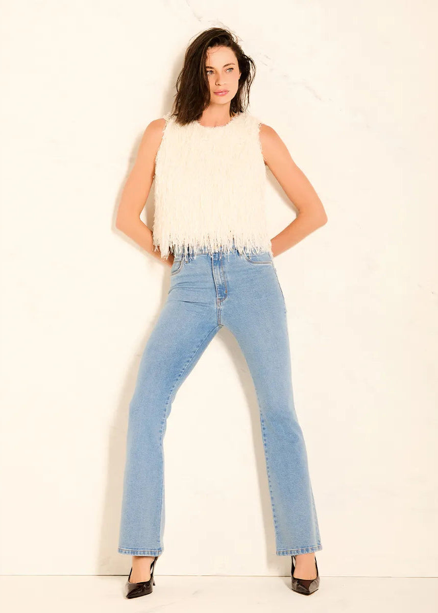 Woman wearing a white sleeveless top and light blue jeans against a plain background