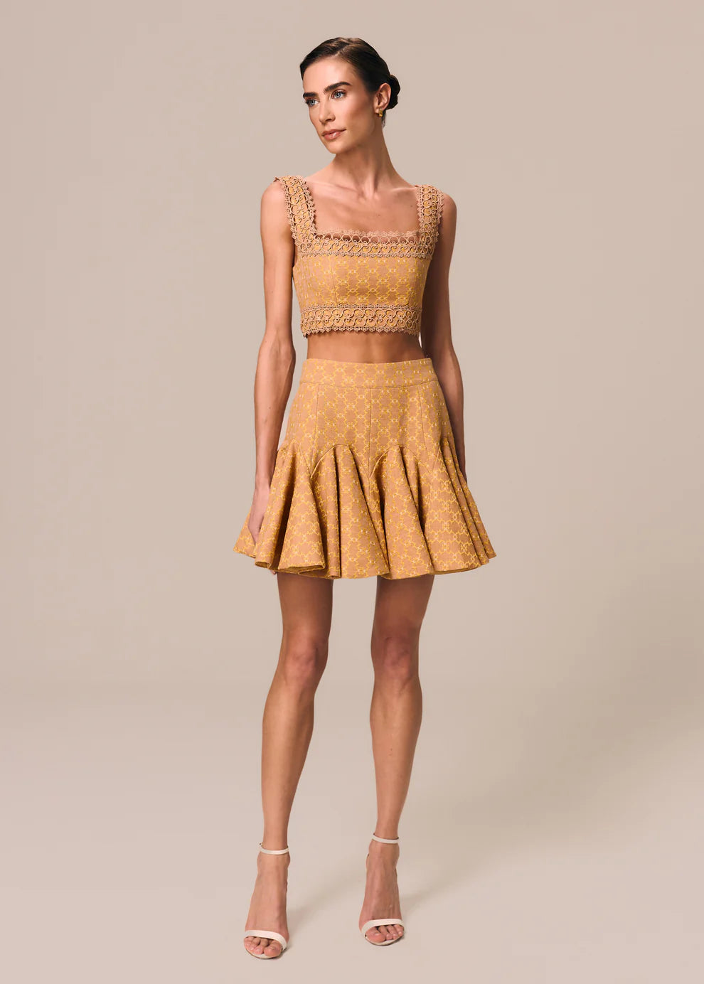 Woman wearing a mustard yellow dress with lace details on a beige background