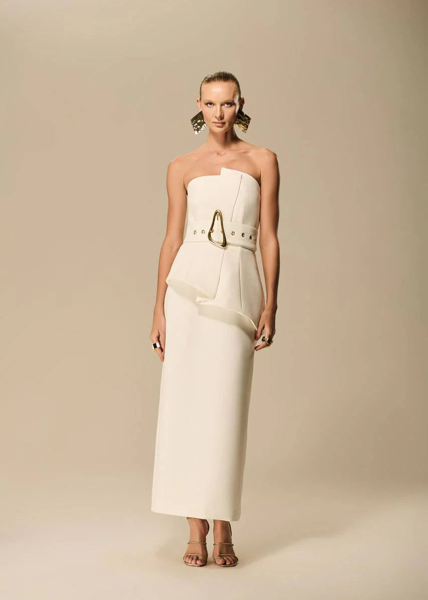 Woman wearing a strapless white dress with a belt against a beige background