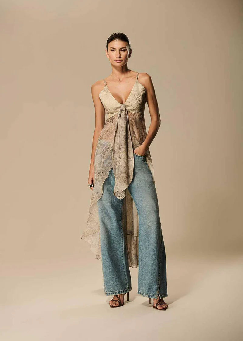 Woman wearing a floral top and denim pants against a beige background