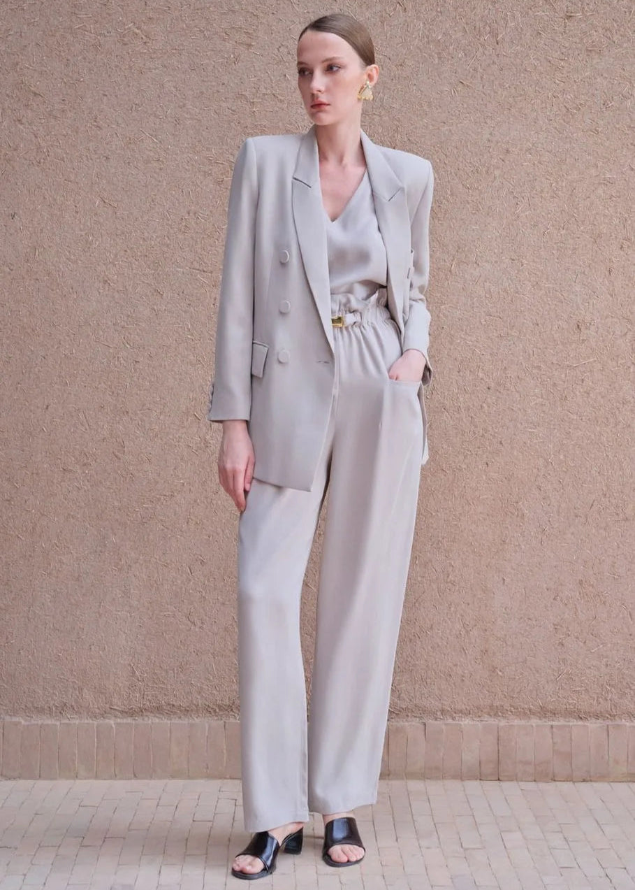 Woman wearing a light gray suit standing against a beige wall.