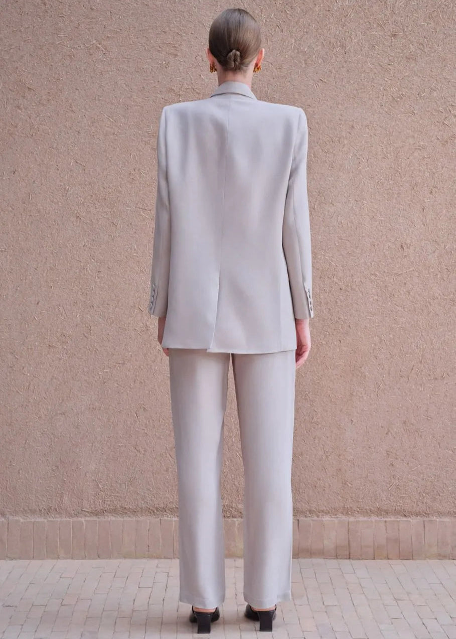 Person wearing a light gray suit standing against a beige wall.