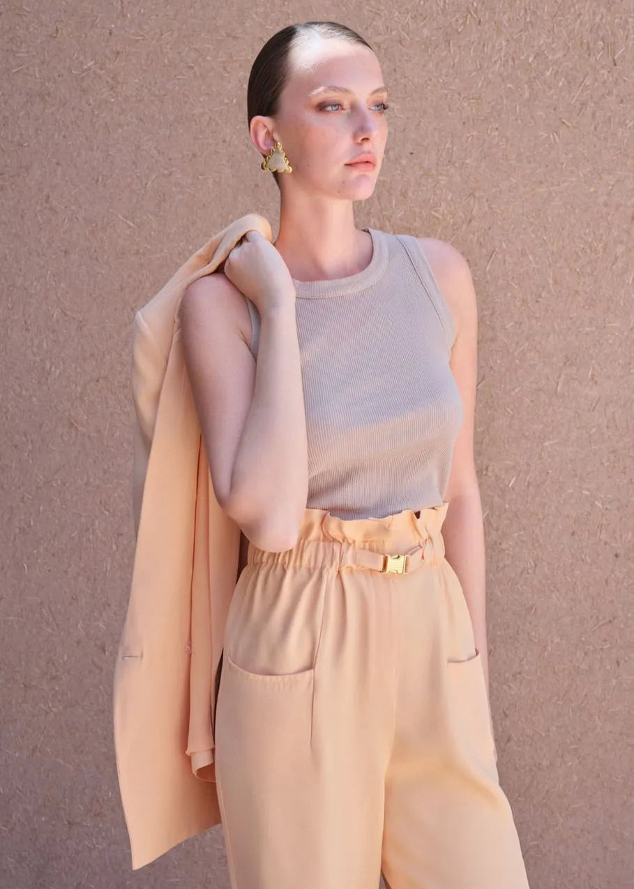 Woman wearing a light gray sleeveless top and beige pants against a beige background