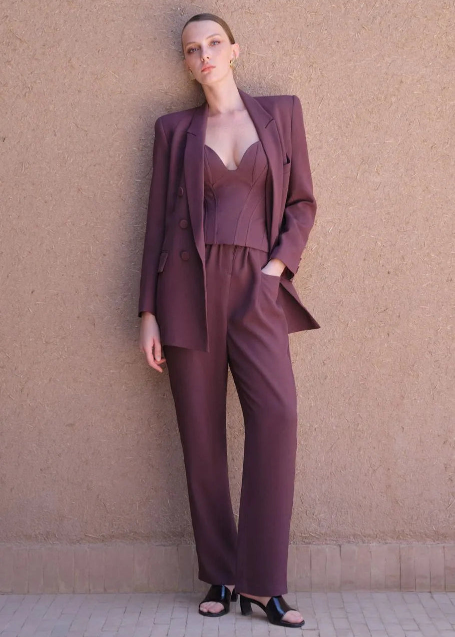 Woman wearing a maroon suit standing against a beige wall.