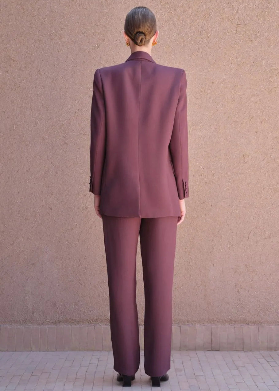 Person wearing a burgundy suit standing against a beige wall.