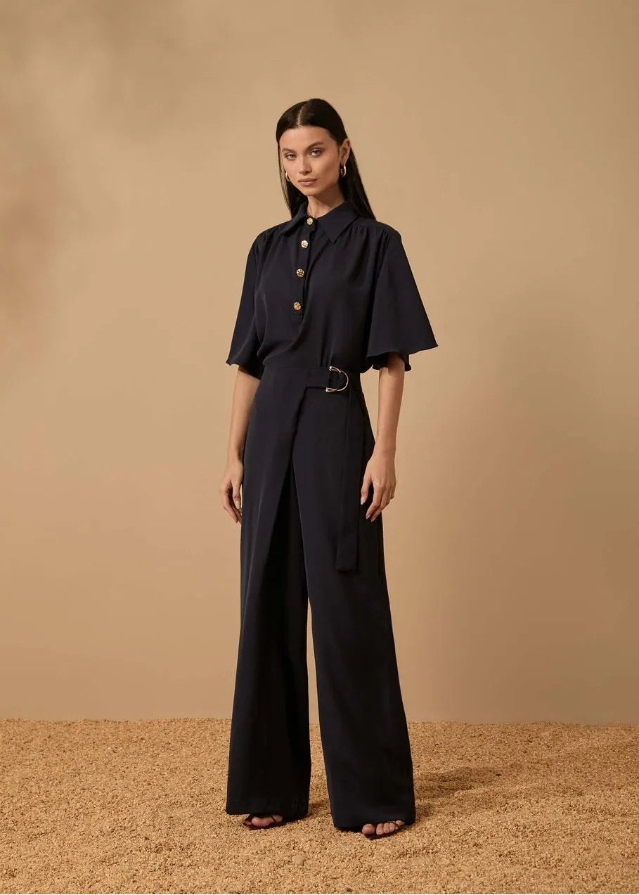 Woman wearing a black outfit with wide-leg pants against a beige background