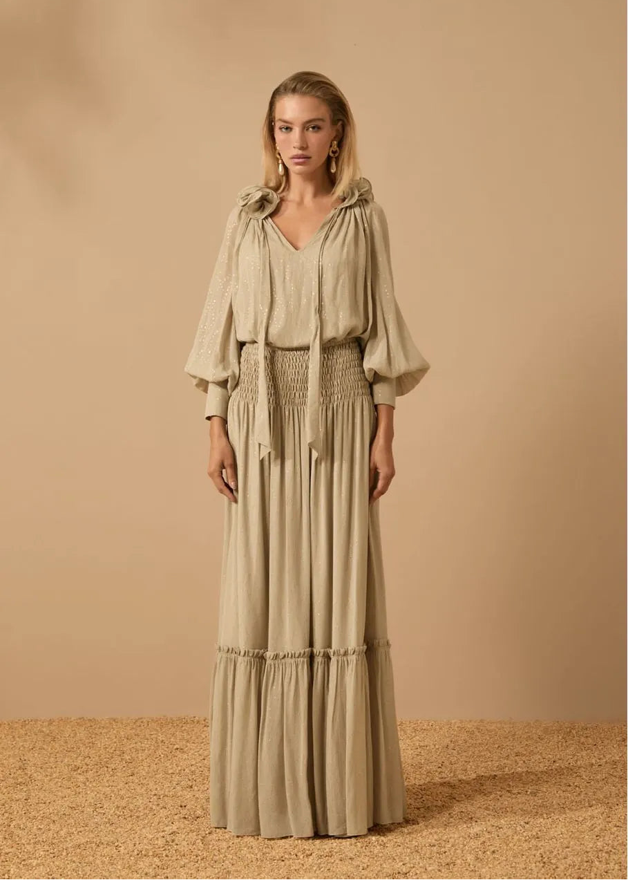 Woman wearing a long, light-colored dress with a matching jacket against a beige background