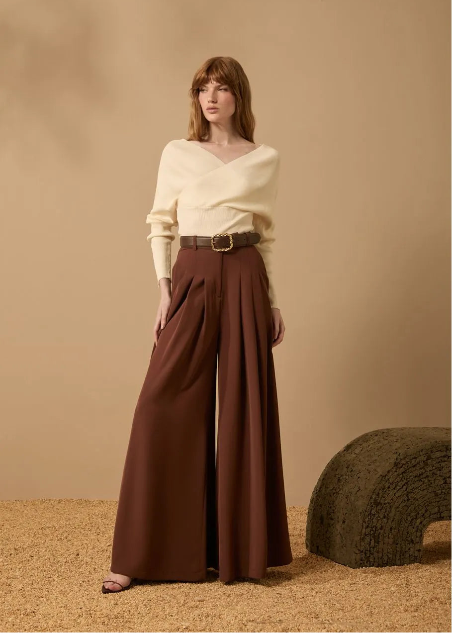 Woman wearing a white top and brown wide-leg pants against a beige background